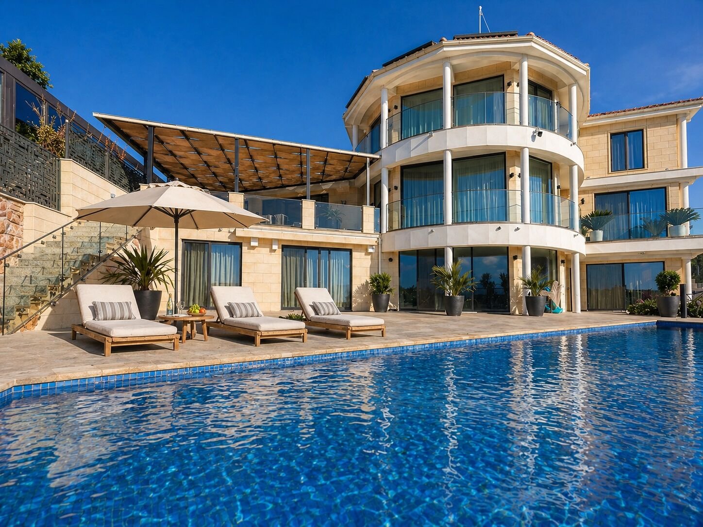 Pool loungers and parasol beside the curved villa façade in bright daylight